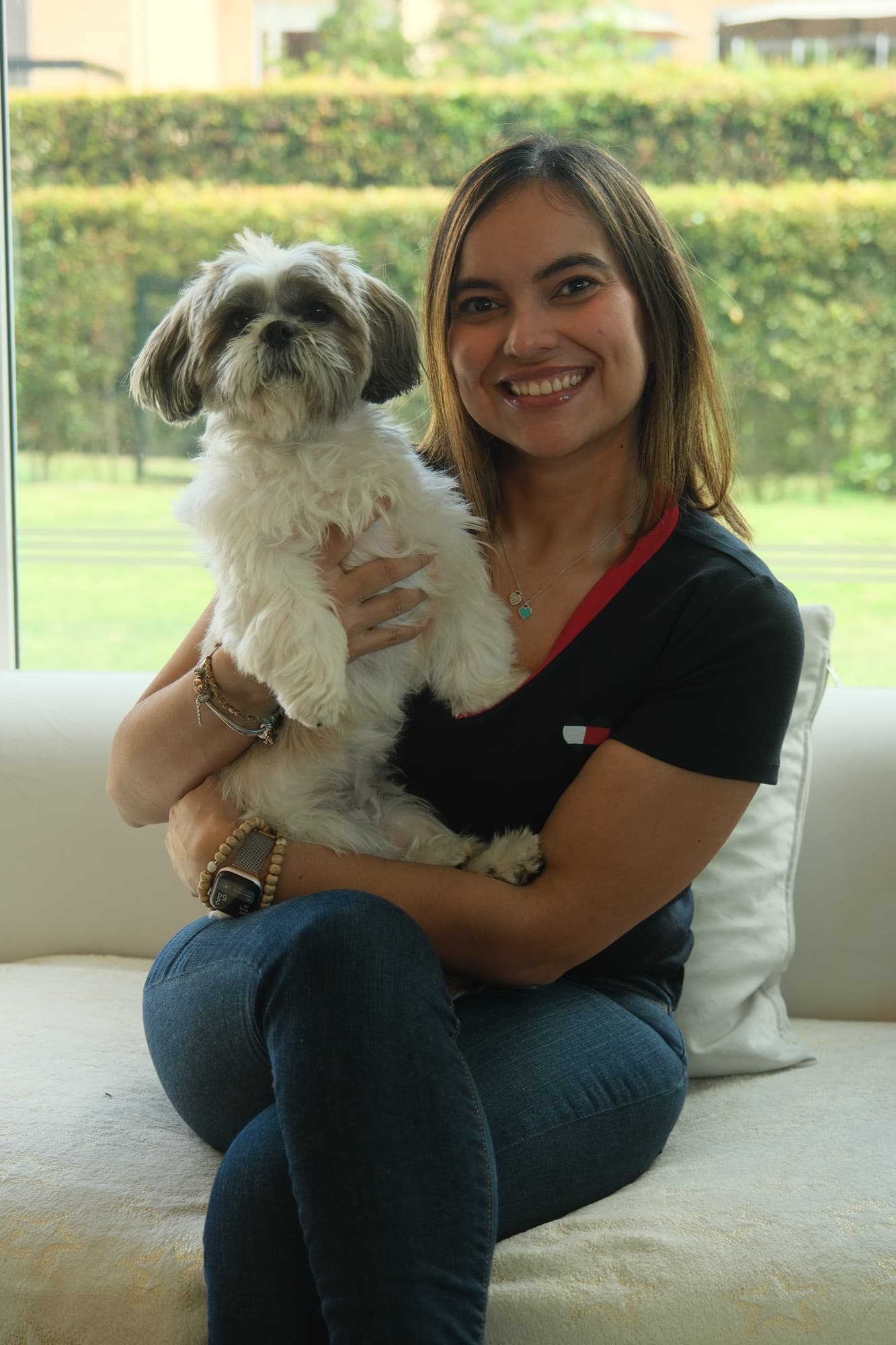 Angélica Cabrera holding her dog, sitting by a large window.